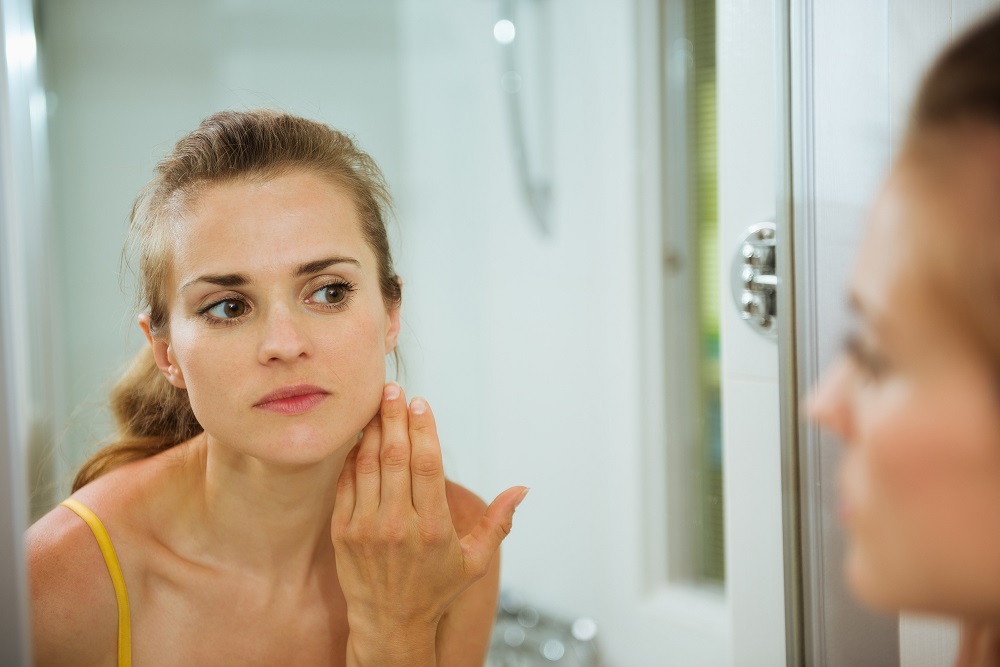 Young woman checking her face in mirror in bathroom