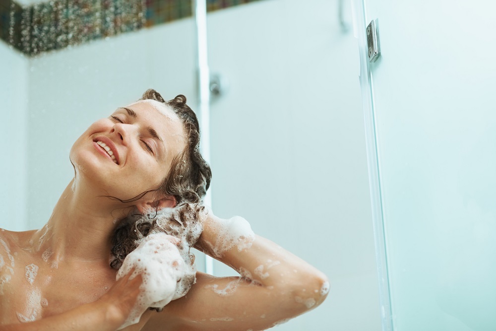 Happy woman washing hair with shampoo under water jet